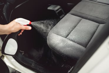 Persona rocía limpiador de tapiz en asiento de vehículo