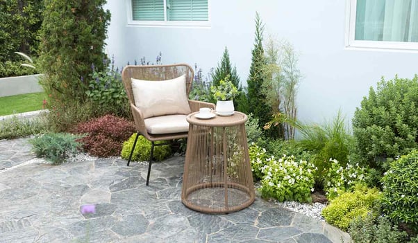 Terraza con piso de piedra y muebles al lado de un pequeño jardín